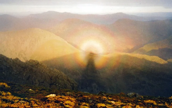 A human shadow surrounded by a colored glory on mountain cloud.