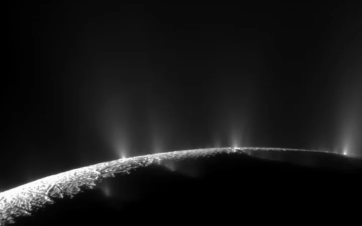Cassini view of bright ice plumes rising from Enceladus against dark space.