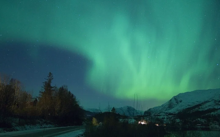 Green aurora borealis above a dark landscape in Norway.
